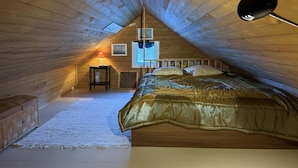 Um quarto de sótão acolhedor com teto inclinado, uma cama de madeira, uma mesinha e uma janela com vista.