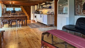 Uma sala de estar aconchegante com piso de madeira, mesa de centro de vidro, sofá preto e um espaço de jantar com cadeiras e mesa de madeira.