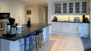 Cozinha moderna com armários brancos, bancada preta e espaço para café.
