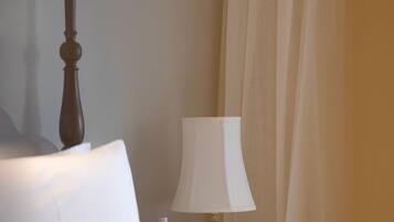 Una cama con un almohadón blanco y un cabecero de madera oscura, una lámpara de noche y una cortina entreabierta.