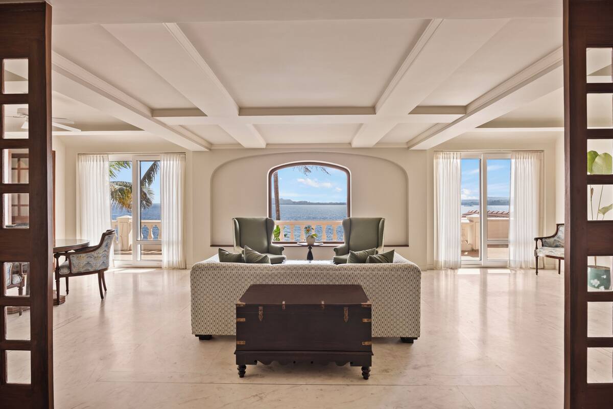 Ein geräumiges Zimmer mit großem Fenster, einem zentralen Tisch und Blick auf den Strand.
