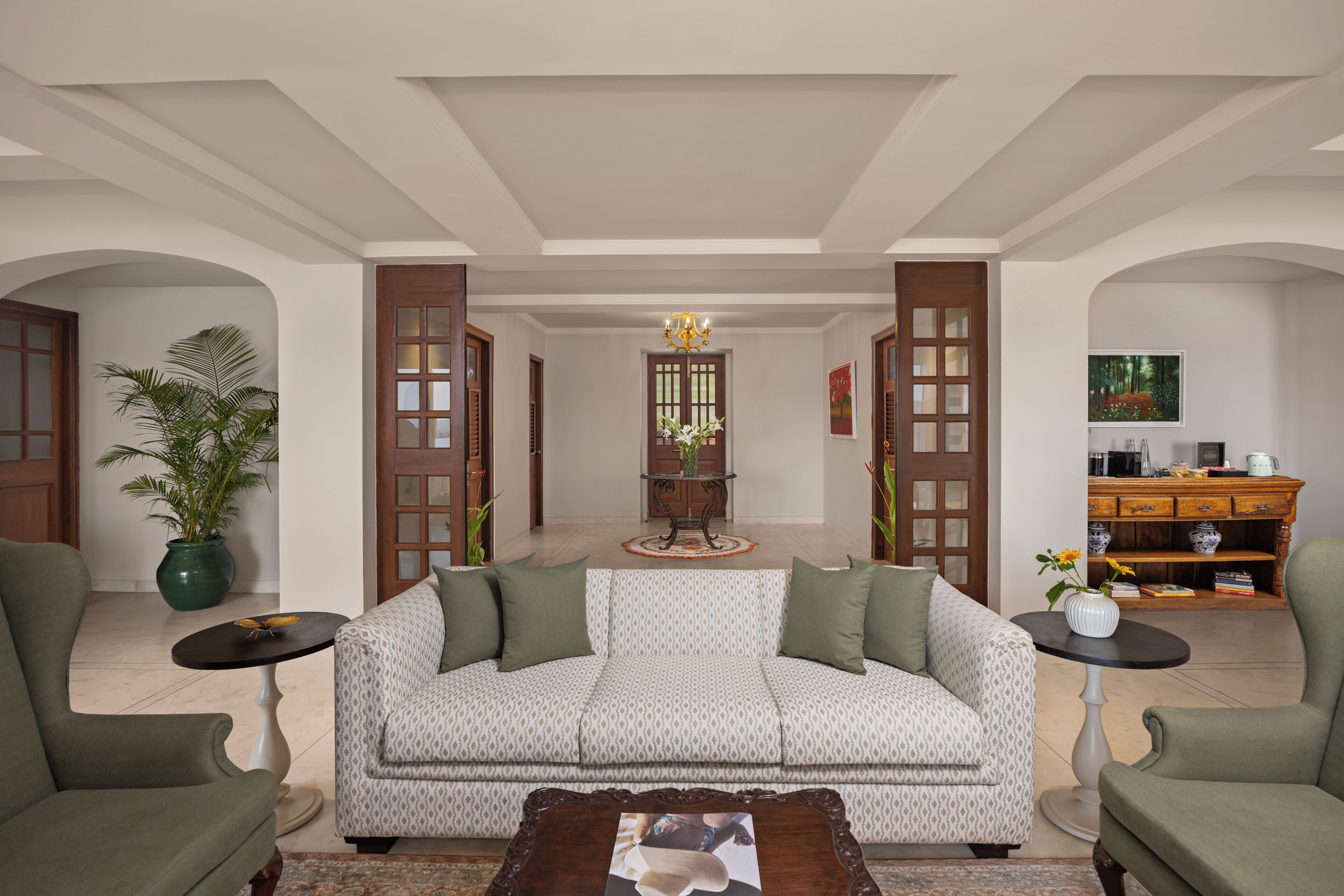 A living room with a patterned sofa, two armchairs, a coffee table, a potted plant, and a wooden cabinet.