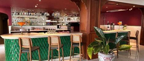 A bar area with a green marble counter, wooden chairs, and a large potted plant.