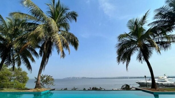 A clear blue pool with palm trees and a view of the sea and airport in the background. - The Postcard on The Mandovi River (Alto de Porvorim)