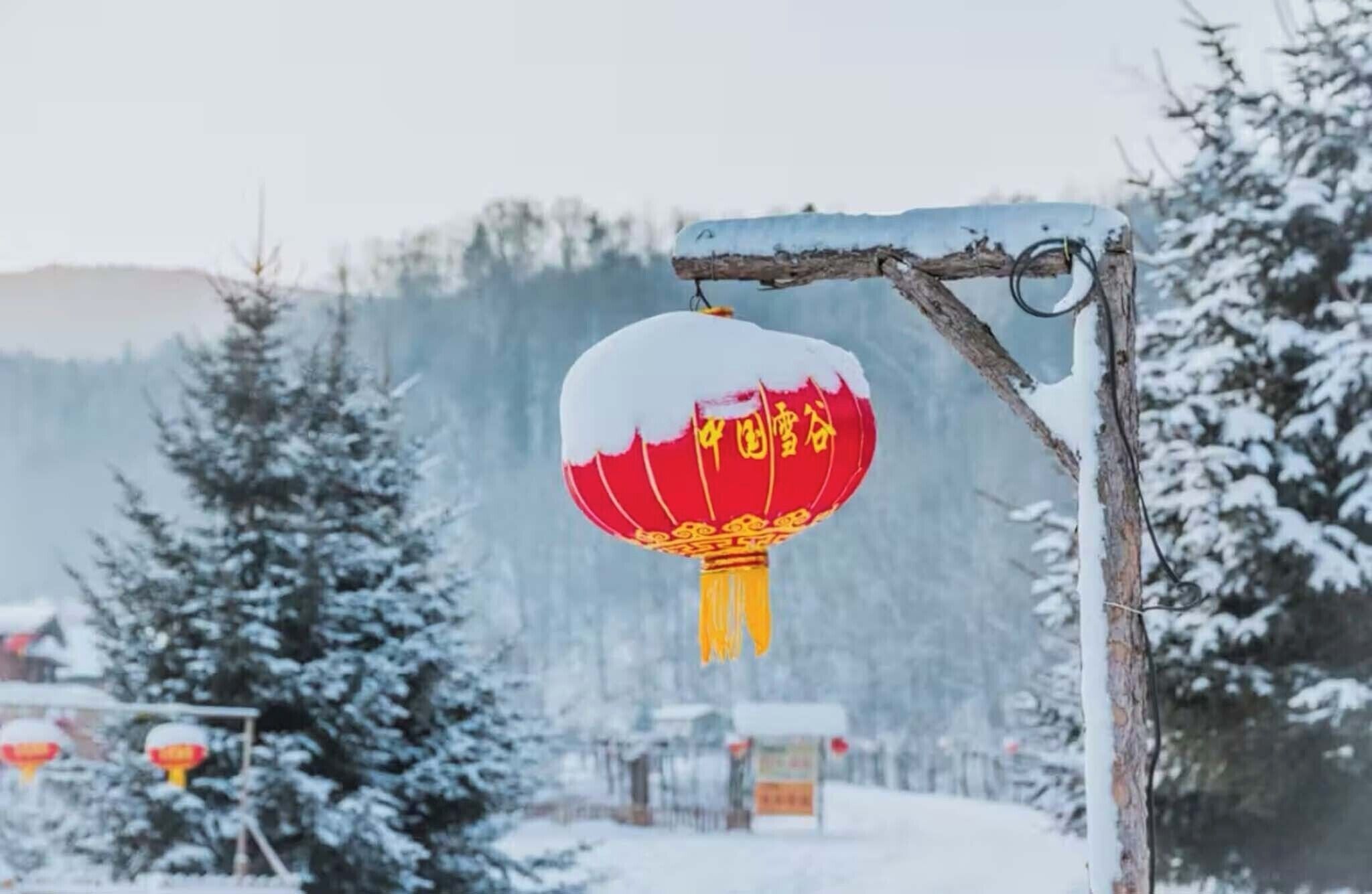 Un farol rojo con caracteres chinos colgado de una estructura metálica en un paisaje nevado.