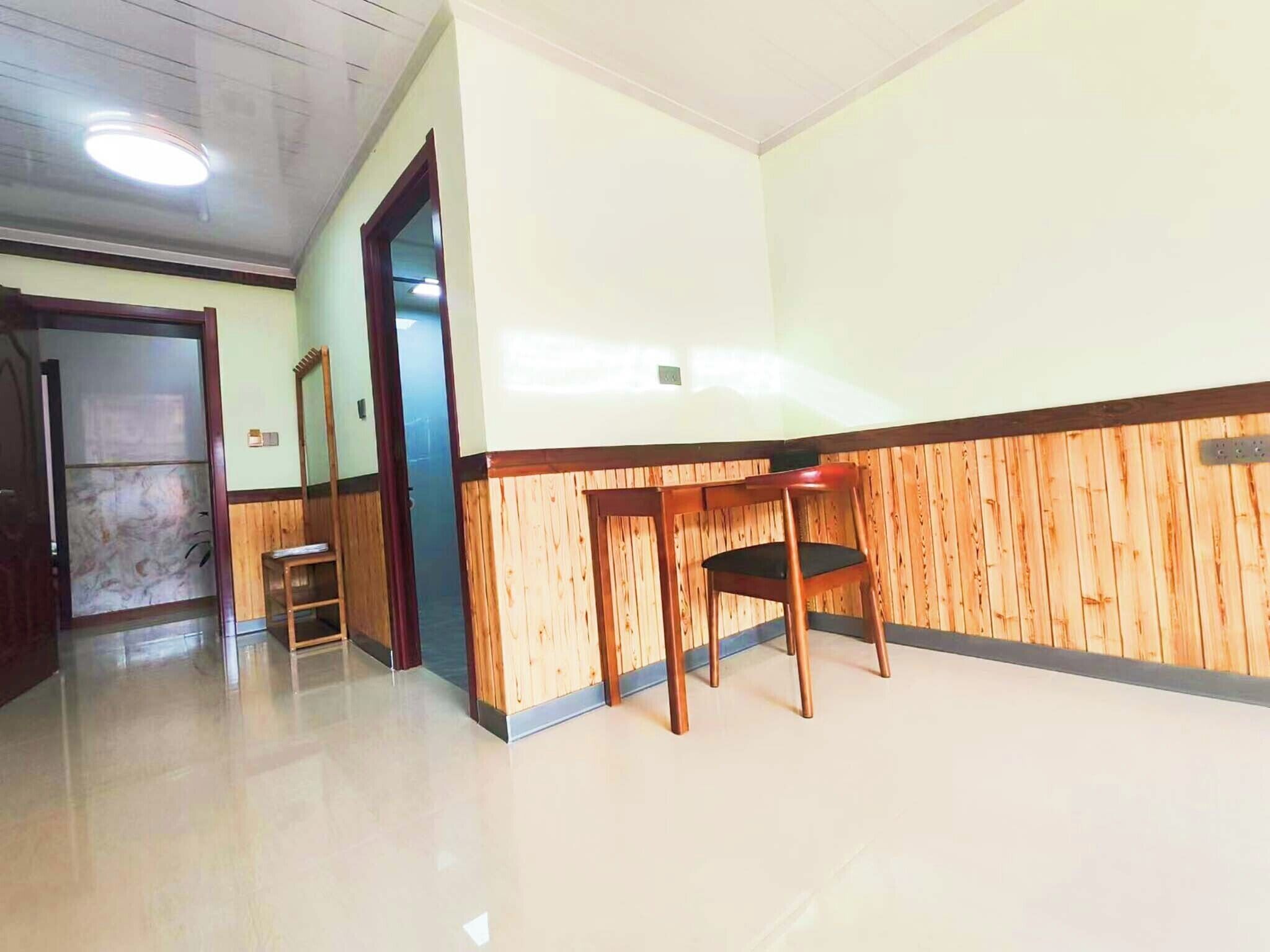 A hotel room with a wooden panel wall, a wooden chair, a small table, and a door leading to another room.