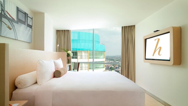 A hotel room with a large bed, a desk, a view of a cityscape, and a framed letter 'h' on the wall. - Horison Ultima Sentraland Semarang (Semarang)