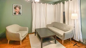 Een kamer met een lichtgroene wand, een witte fauteuil, een bank, een kleine tafel en een vloerlamp.
