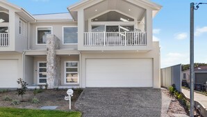 A two-story house with a white exterior, a balcony on the upper floor, and a garage. - Ruby Jade Coastal Luxury at Anna Bay (Anna Bay)