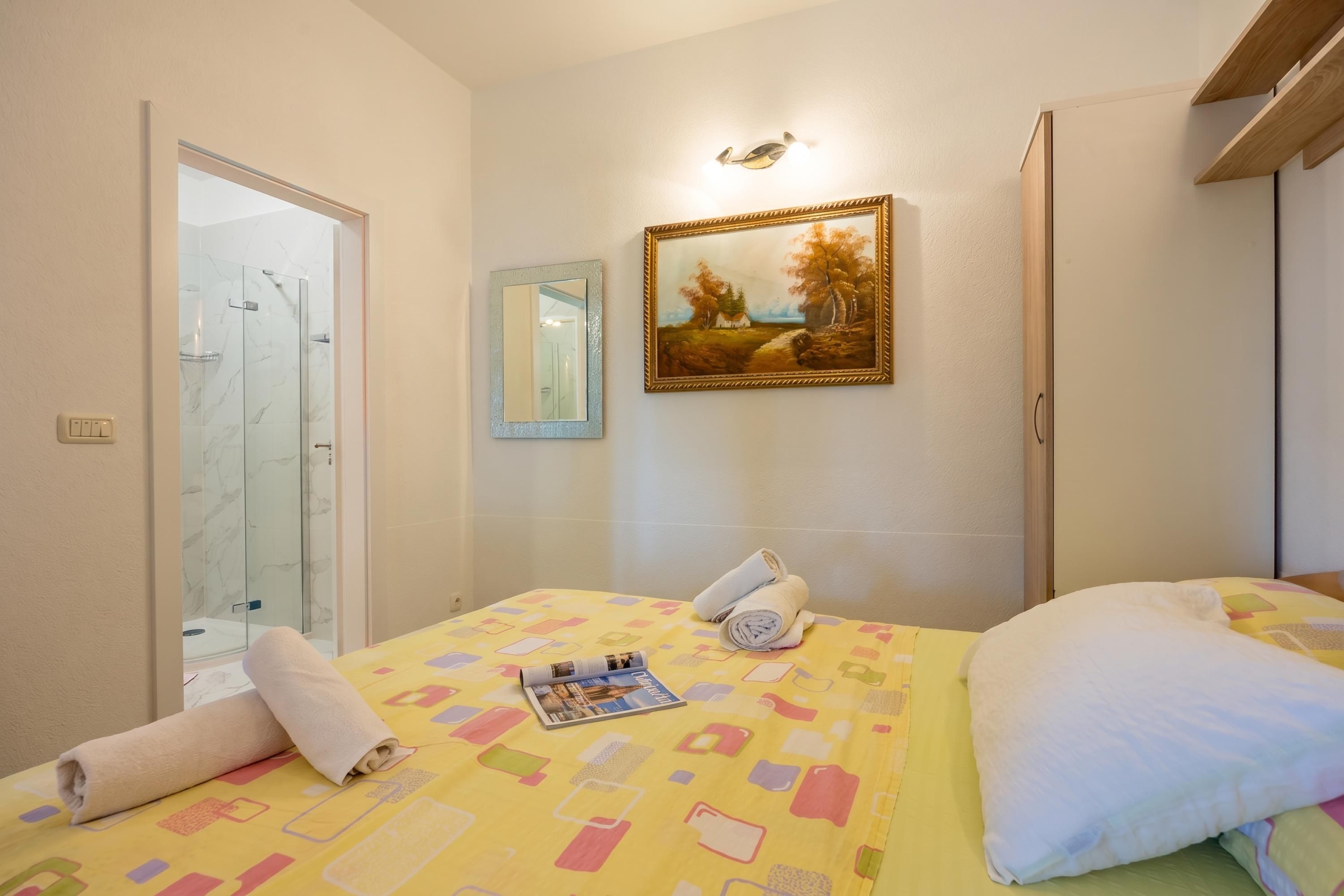 A hotel room with a bed, a painting, a shower, and a door.