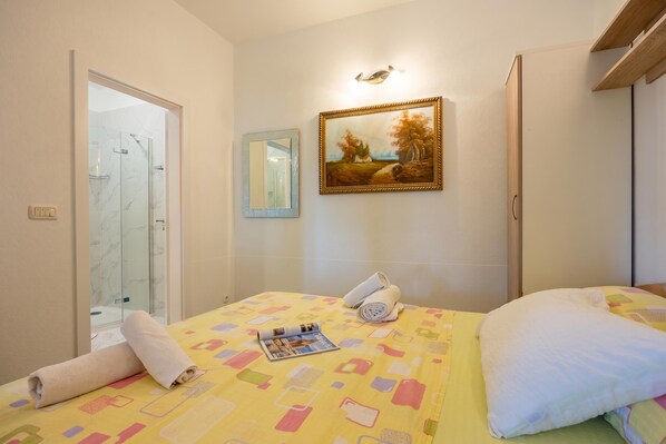 A hotel room with a bed, a painting, a shower, and a door.