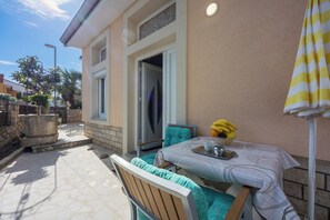 Eine Terrasse mit Tisch für zwei Personen, einem Stuhl und einem gelb-gestreiften Sonnenschirm.