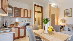 A modern kitchen with a dining area, including a wooden table, chairs, and a fruit bowl. - Amalija Sea View Studio  Apartment 4, Mali Lošinj, Croatia (Mali Lošinj)