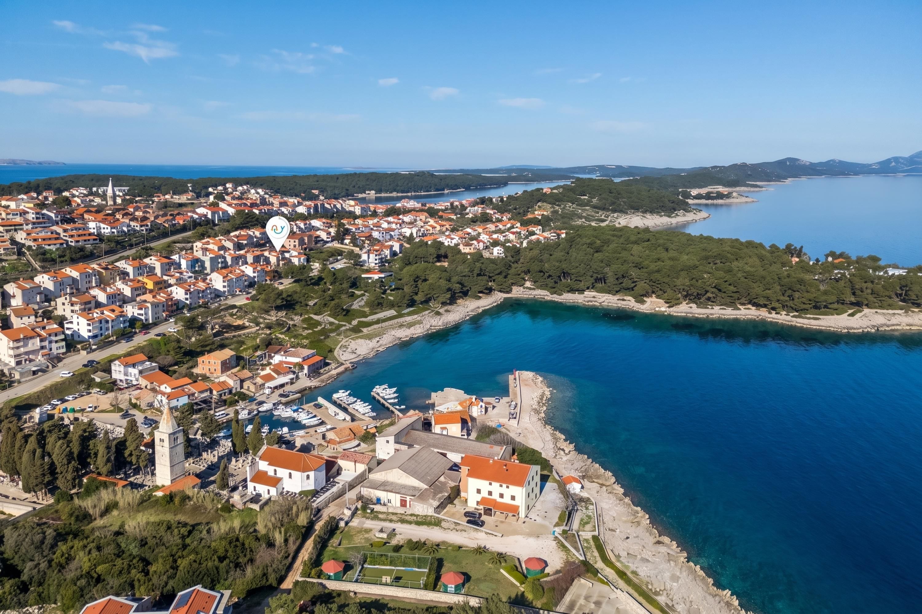 An aerial view of a coastal town with a marina, residential buildings, and a prominent church.
