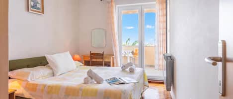 A hotel room with a bed, a chair, a table, a window, and a door.