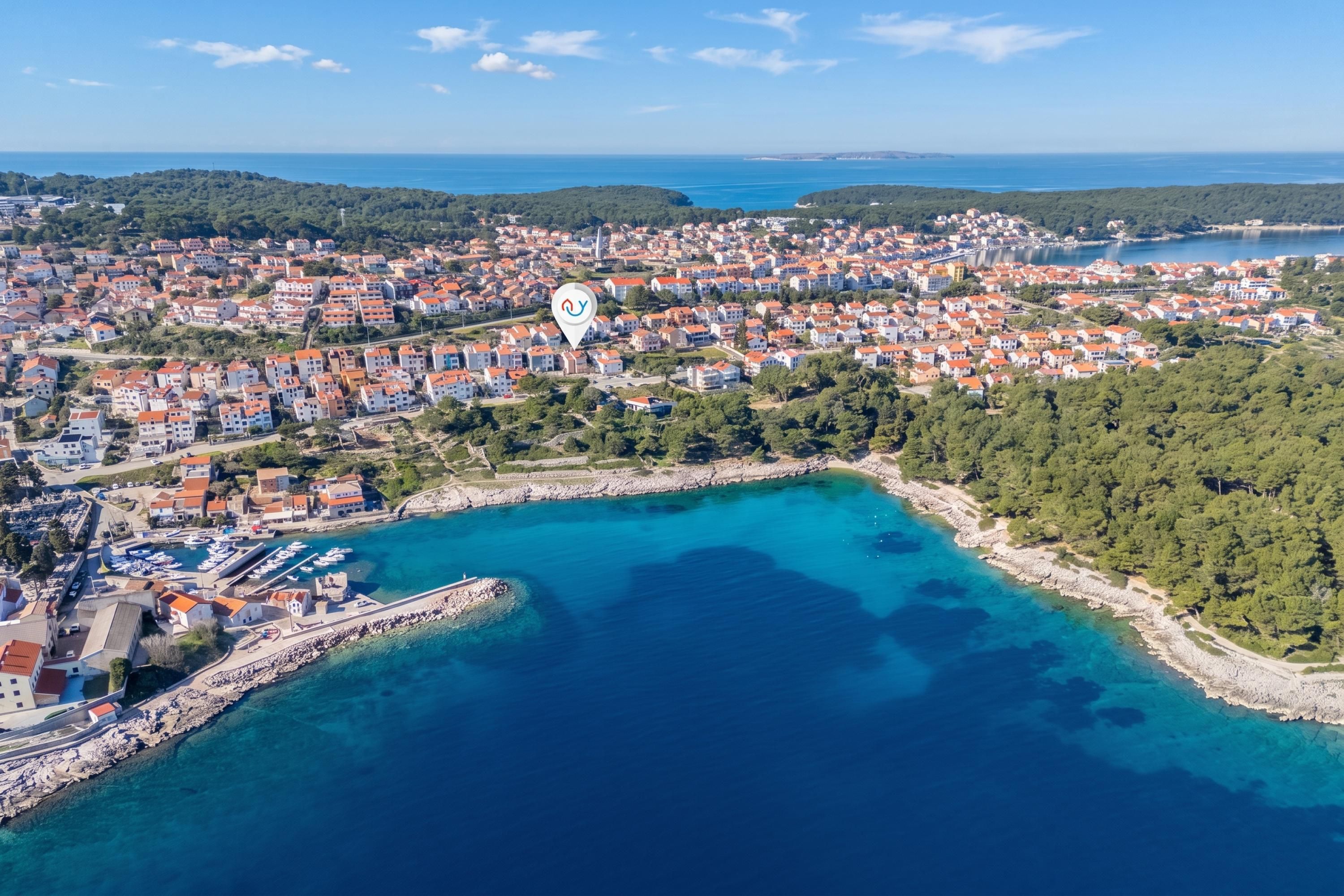 An aerial view of a coastal town with a marina, dense residential area, and a clear blue sea.