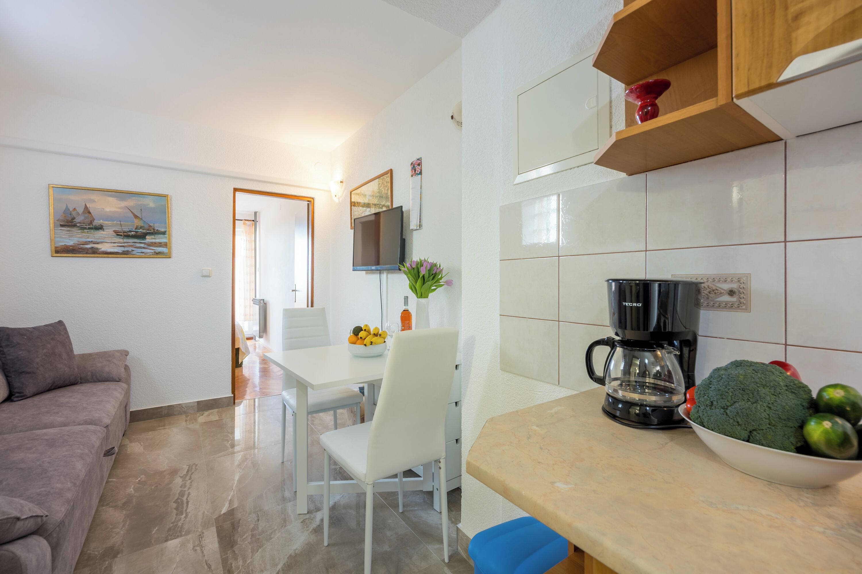 Een moderne keuken met een koffiezetapparaat, een fruitschaal en een eethoek met een witte tafel en stoelen.