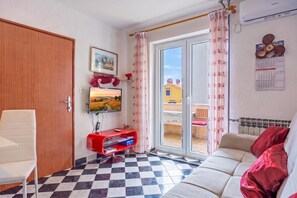 Ein Zimmer mit Schachbrettmuster-Bodenbelag, einer Couch, einem Fernseher, einer Tür und einem fenster mit Vorhängen.