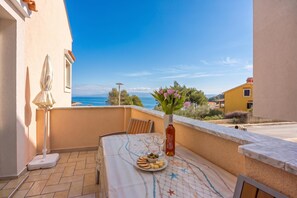 A balcony with a table set for two, a vase with flowers, and a view of the sea.