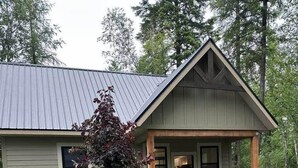 Une maison de plain-pied avec un porche couvert, un petit arbre et une allée gravillonnée.