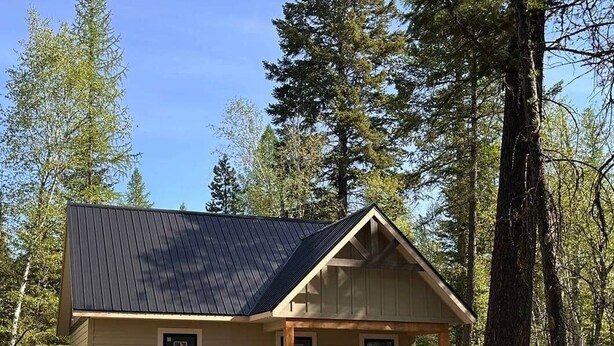Une petite cabane d’un seul étage, avec un toit sombre, un revêtement de couleur beige et un porche à l’avant.