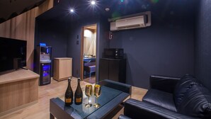 A modern living area with a glass table, a black leather sofa, a kitchen area with a microwave, and a staircase. - hoteru saphir (Toyama)