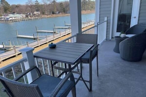 Een overdekt buitengebied met een tafel en stoelen, met uitzicht op een waterpartij en liggende boten.