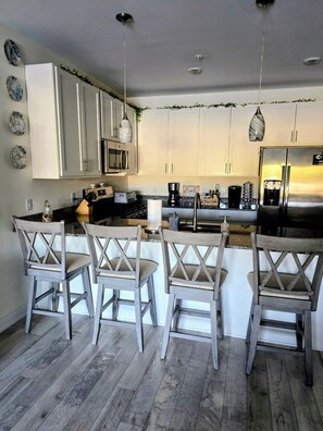 A modern kitchen with white cabinets, a stainless steel refrigerator, and a bar area with wooden chairs.