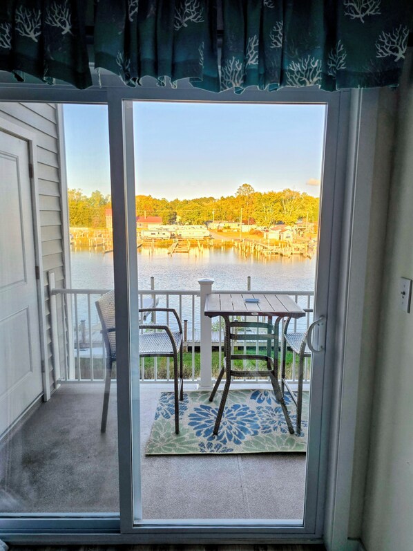 A balcony with a table and chairs, overlooking a body of water with buildings and trees in the background.
