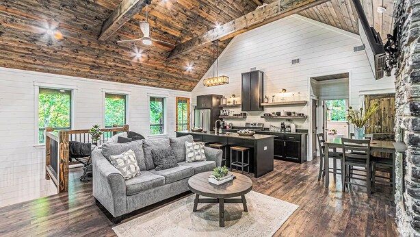 A spacious living room with a large gray sofa, a coffee table, and a kitchen area with a bar and island. - Private Creek Cabin with Hot Tub, Bunk Room and Game Room (Broken Bow)