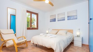 A bedroom with a bed, a rocking chair, a nightstand, and a ceiling fan. - PUNTA LLARGA - Cozy house with sea views, private pool and free Wi-Fi (Artà)
