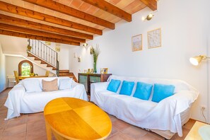 A room with a wooden ceiling, a staircase, a white sofa, a wooden table, and a dining area. - PUNTA LLARGA - Cozy house with sea views, private pool and free Wi-Fi (Artà)