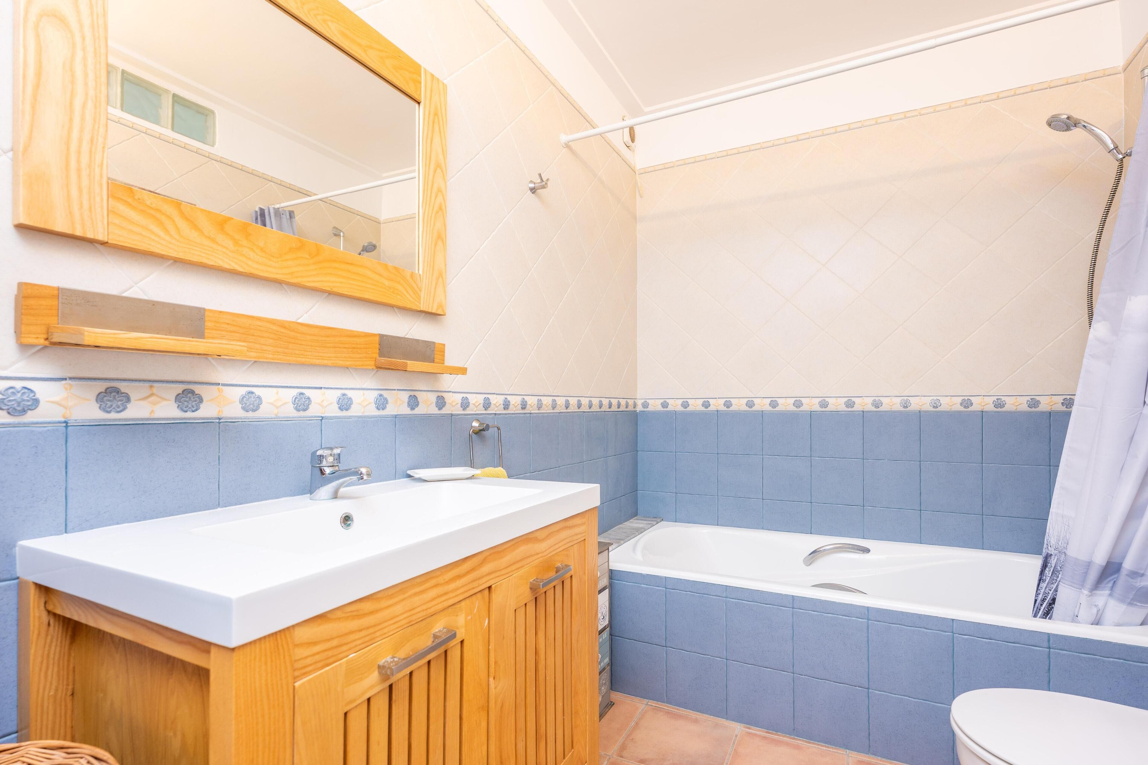 Ein Badezimmer mit einem Holzbadschränken, einem weißen Waschbecken, einer Badewanne und einer Dusche.