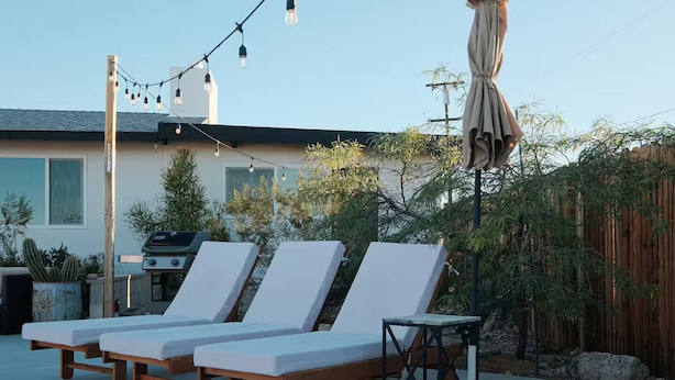 Un patio con tres sillones blancos, una parrilla y luces colgantes.