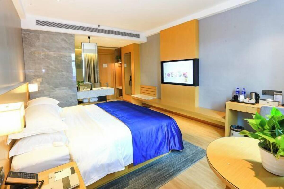 A hotel room with a bed, bedside table, desk, chair, and a TV mounted on the wall.