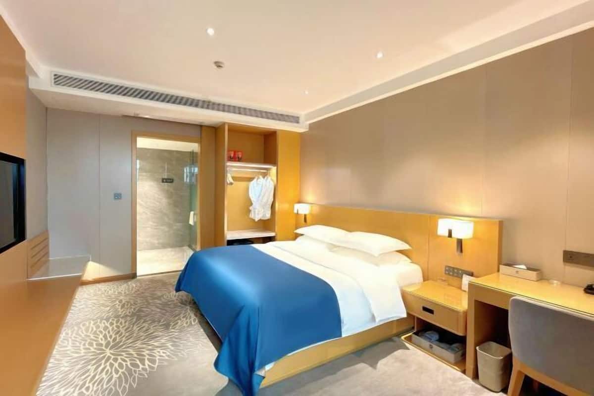 A hotel room with a bed, bedside table, lamp, desk, chair, and a wardrobe.