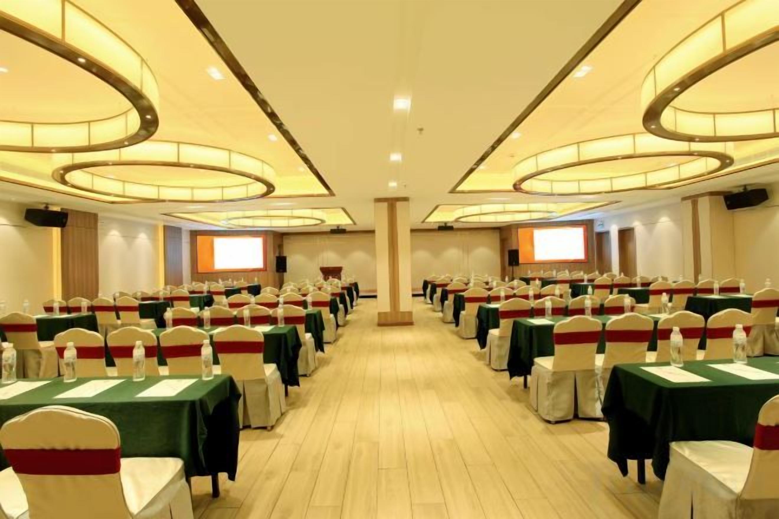 Une salle de conférence avec des rangées de tables, des chaises et un grand écran à l’avant.