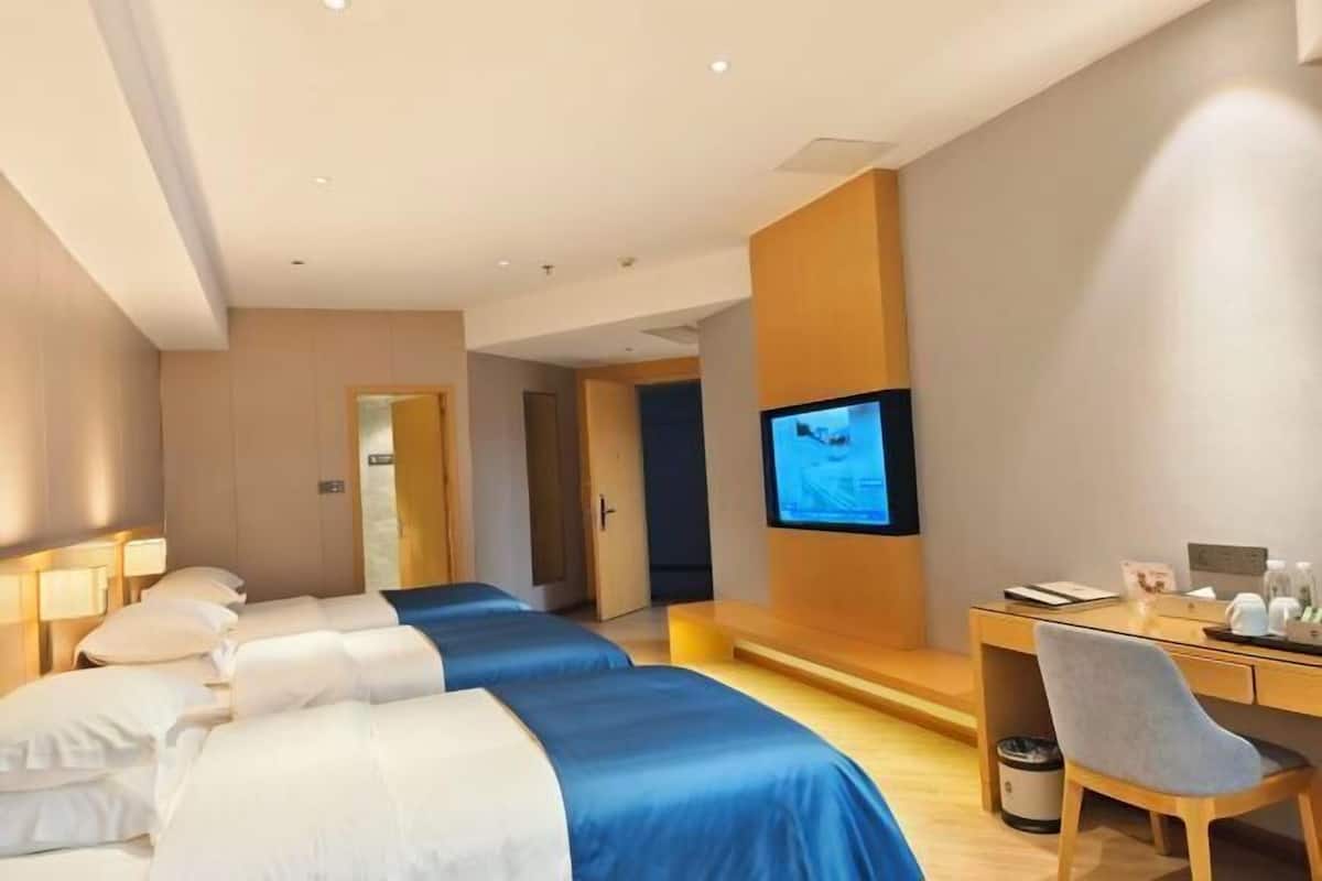 A hotel room with two beds, a desk, a chair, a television, and a trash can.