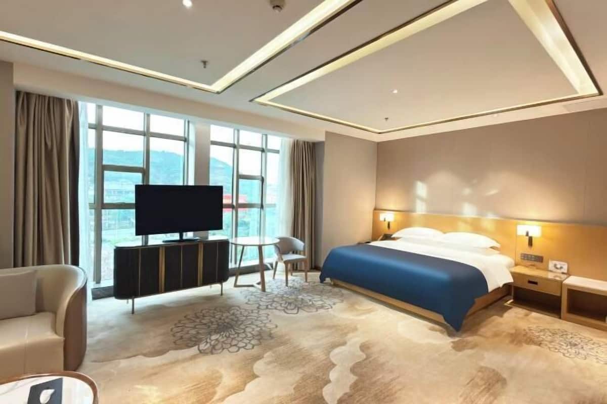A hotel room with a bed, a TV, a desk, and a view of the outdoors.