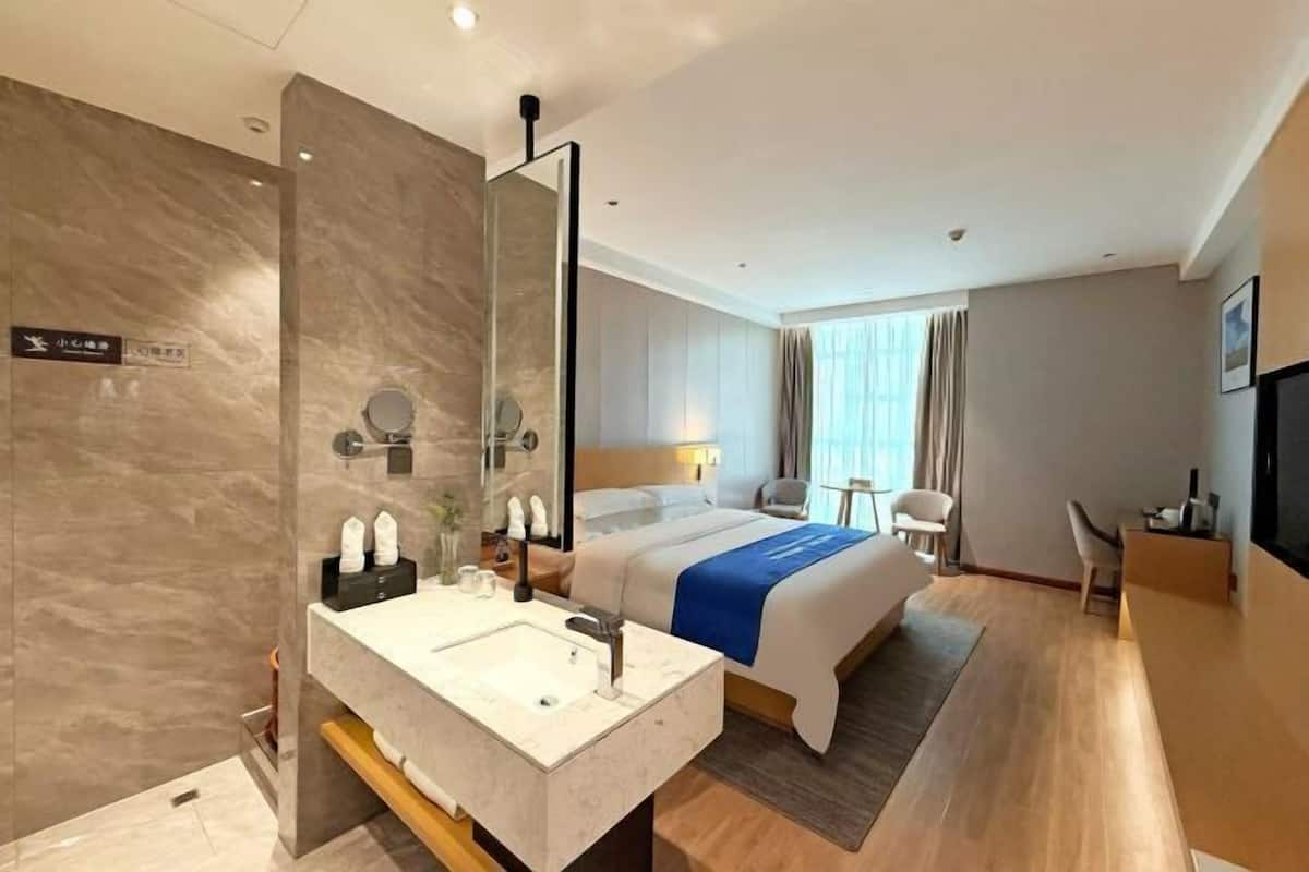 A hotel room with a large bed, a bathroom with a mirror and sink, a desk, and a TV.