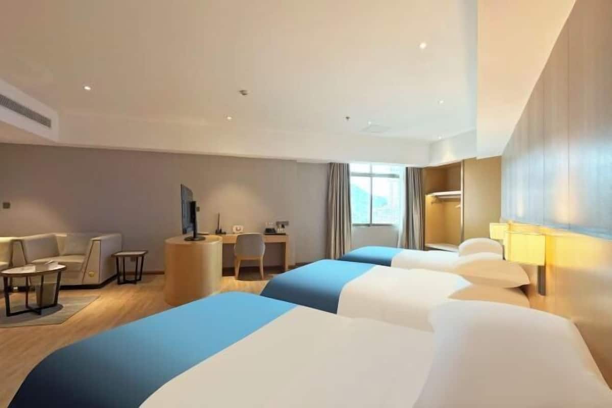 A hotel room with three beds, a desk, a chair, and a TV.