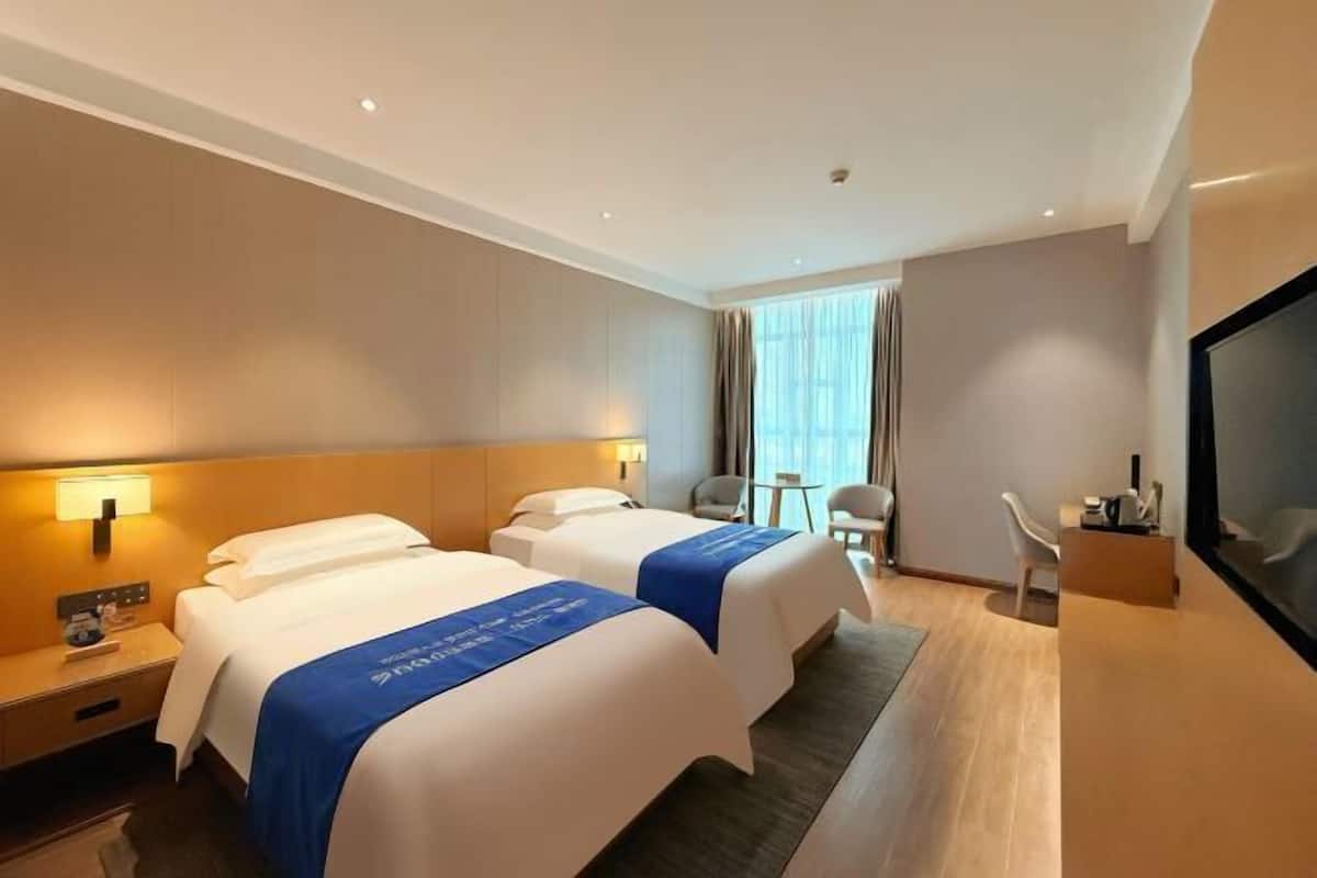 A hotel room with two beds, a TV, a desk, and a chair.