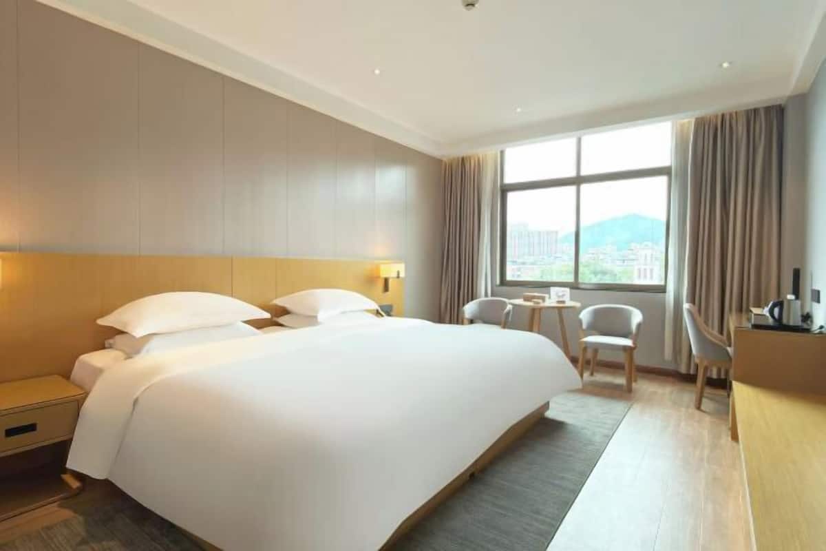 A hotel room with a large bed, a desk, a chair, and a window with a city view.