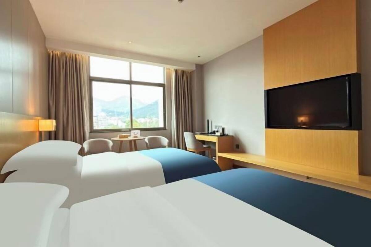 A hotel room with two beds, a desk, a chair, a TV, and a window with curtains.