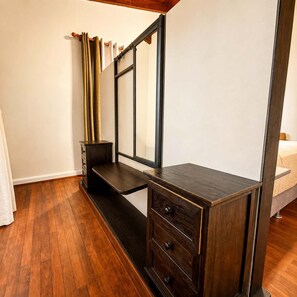 Ein Zimmer mit einem dunklen Holzschrank, einem Spiegel und einem Bett mit weißer Matratze.