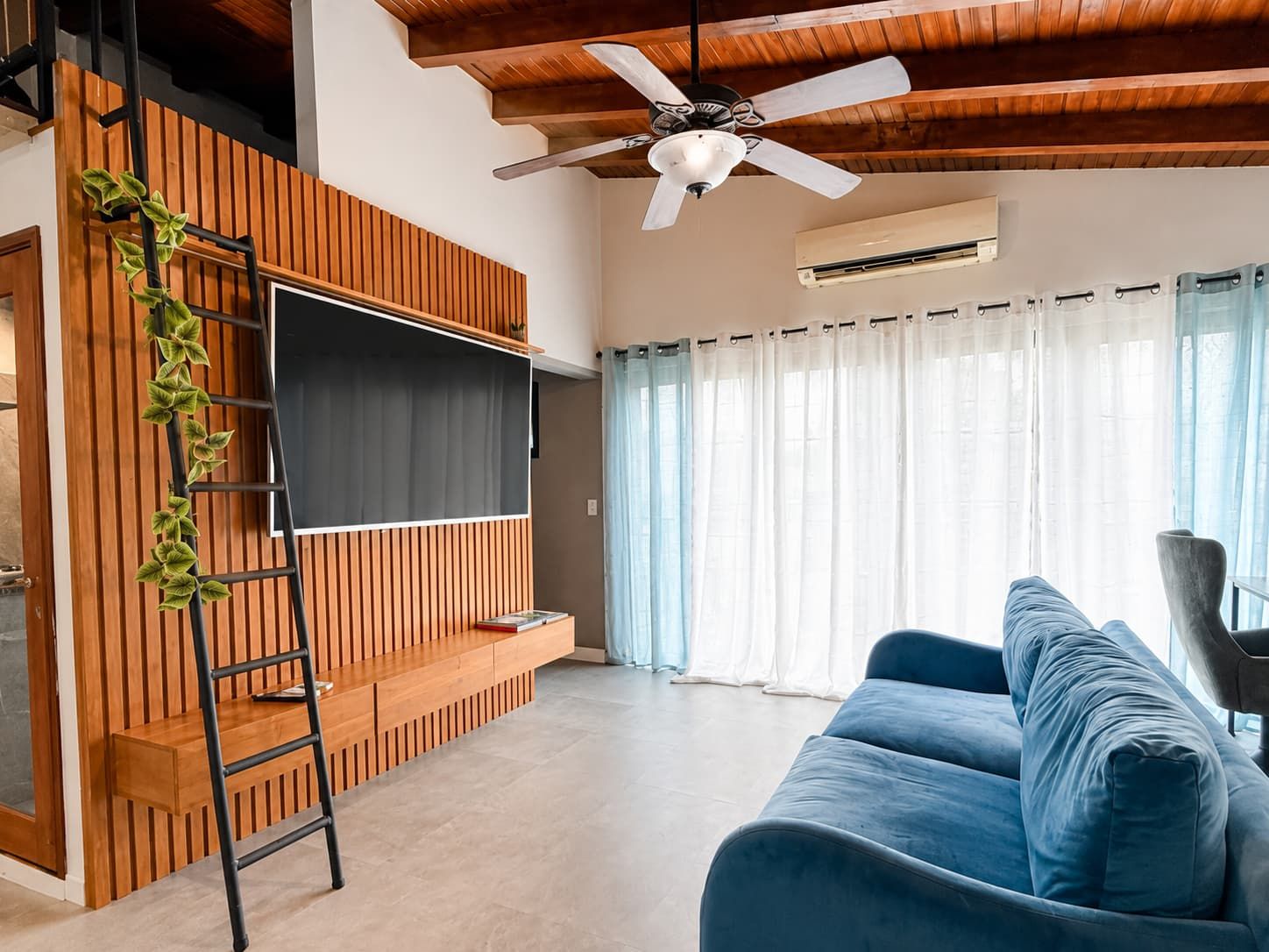 Una sala de estar moderna con un sofá azul, un televisor montado, un ventilador de techo y una pared de listones de madera.