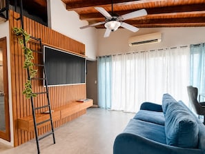 Ein modernes Wohnzimmer mit einem blauen Sofa, einem Wand-Fernseher, einem Deckenventilator und einer Wandverkleidung aus Holzleisten.