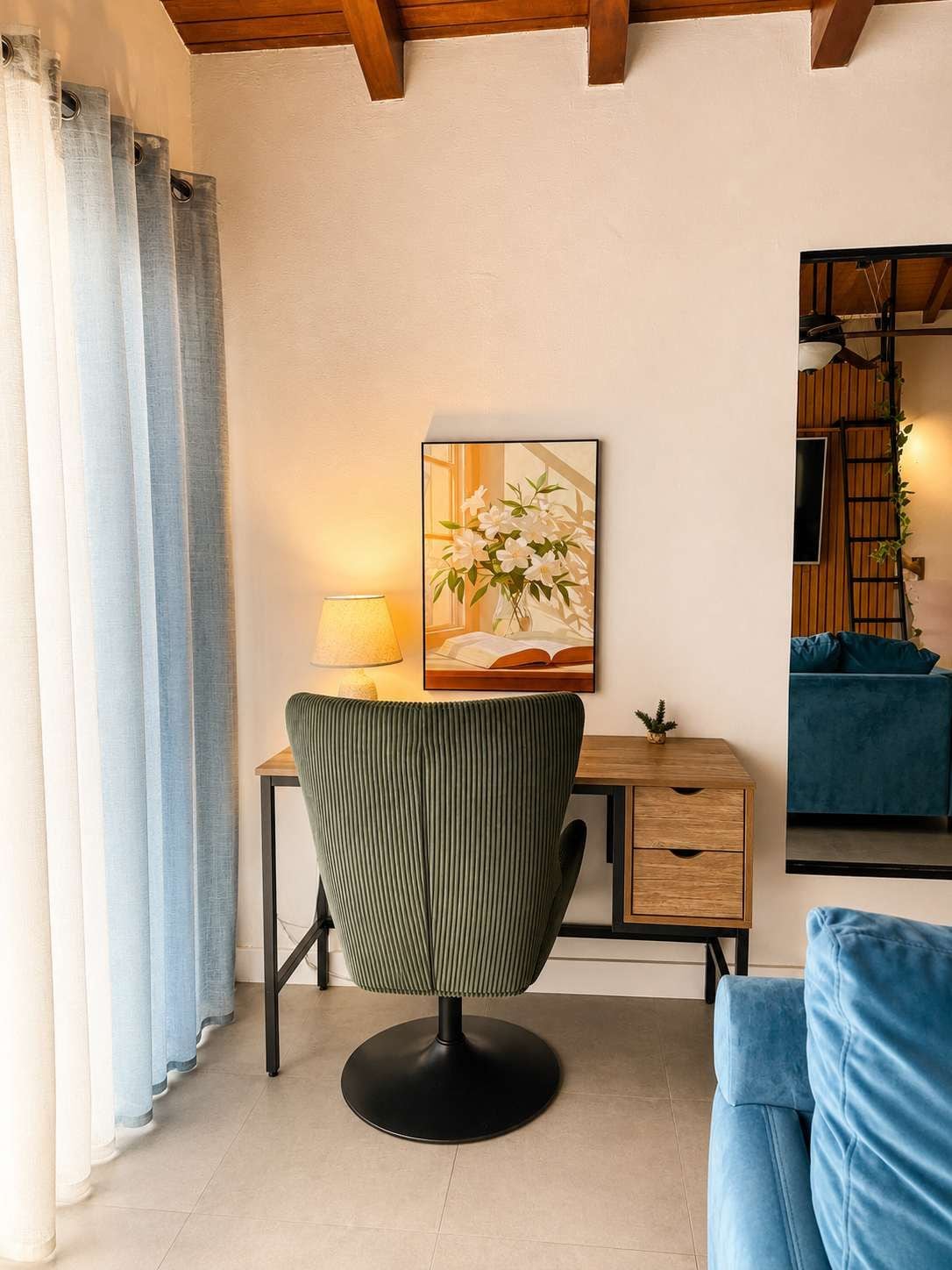 Une pièce comprenant un bureau, une chaise et un canapé bleu. Il y a un tableau au mur et une lampe sur le bureau.