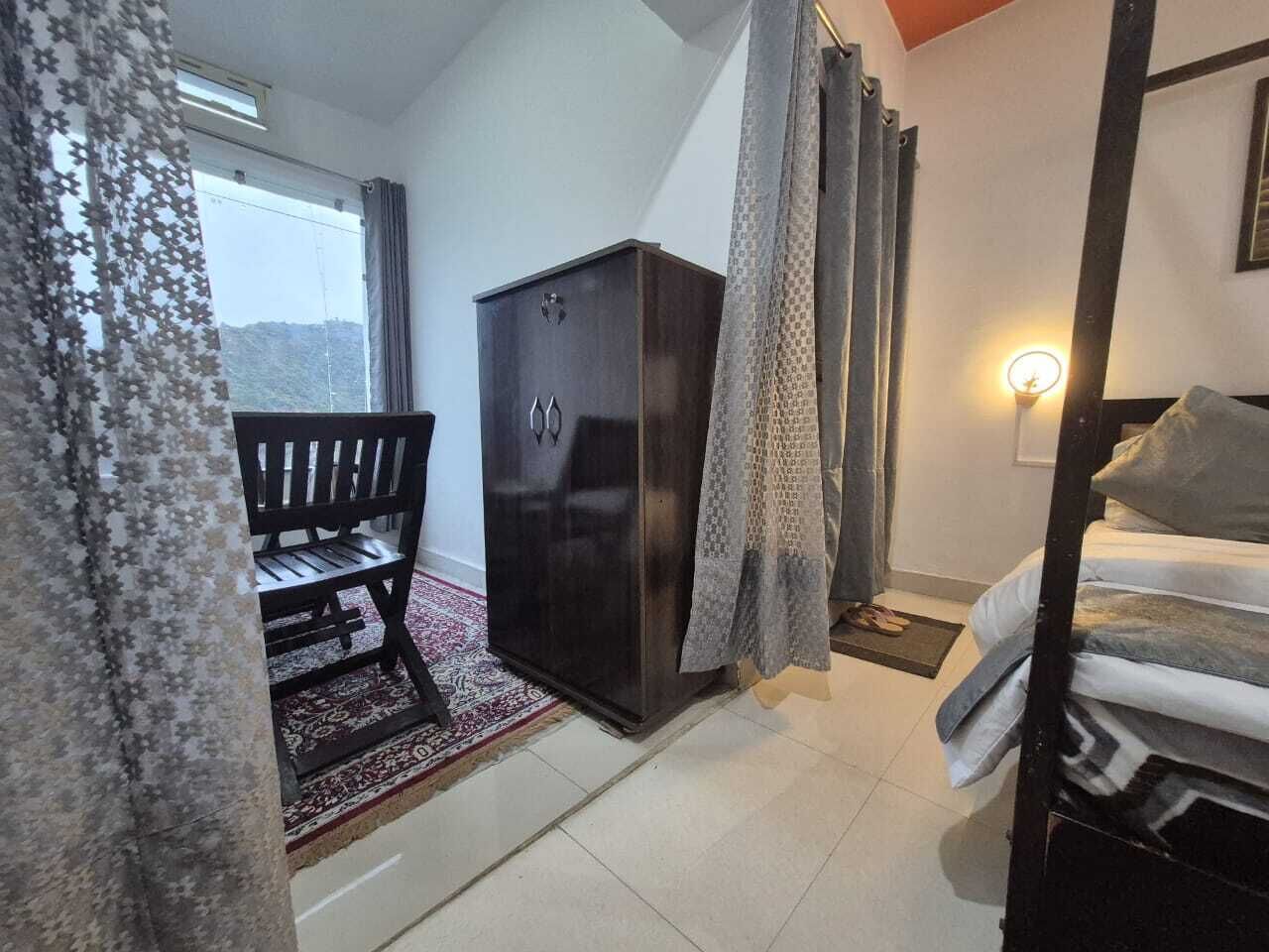 Una habitación con cama, armario, banco y ventana con cortinas.