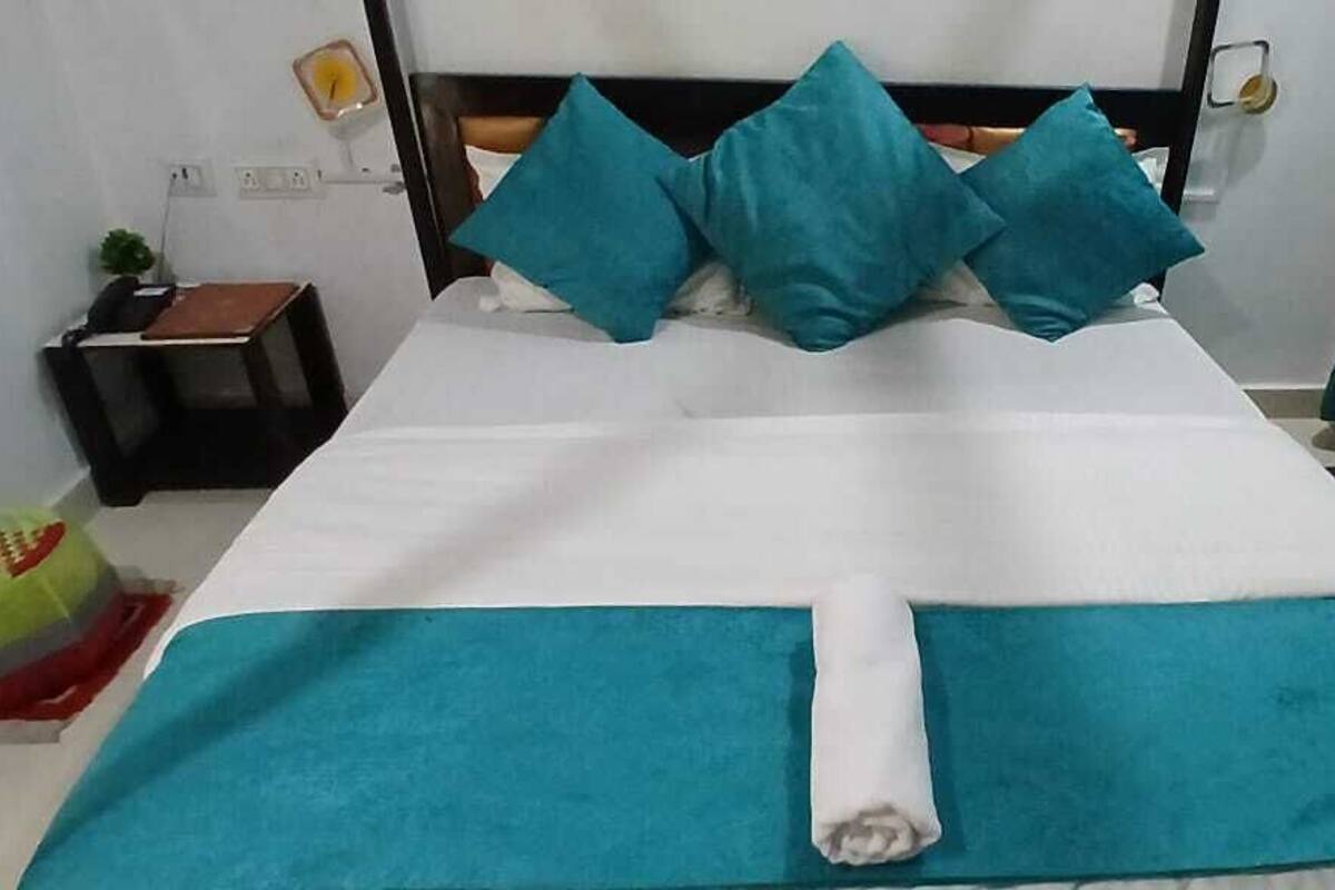 Een net opgemaakt bed met smaragdgroene en witte beddengoed, een houten hoofdbord en smaragdgroene gordijnen.
